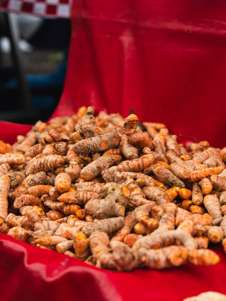 Freshly harvested turmeric roots displayed on red cloth at a local outdoor market.